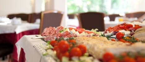 Una mesa de buffet con diversos alimentos y un gran plato de carnes en rodajas.