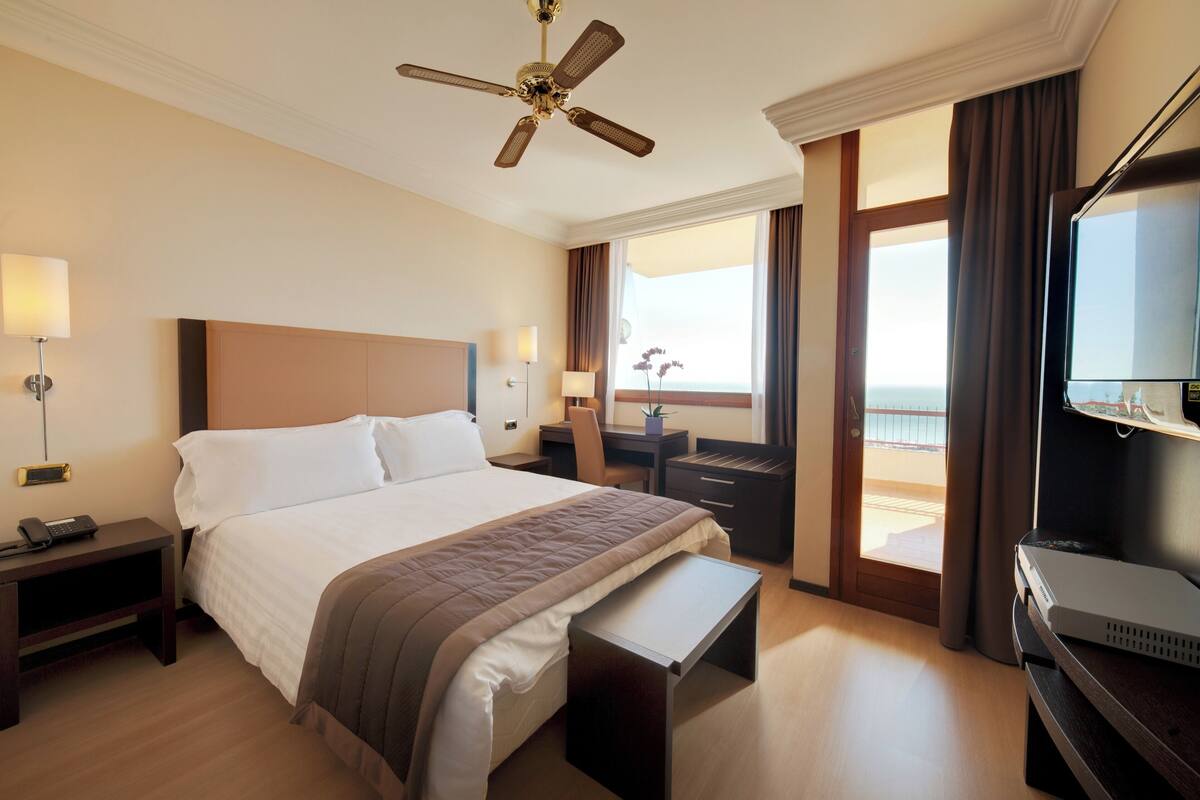 Ein Hotelzimmer mit Bett, Nachttisch, Lampe, Schreibtisch, Stuhl und Fernseher.
