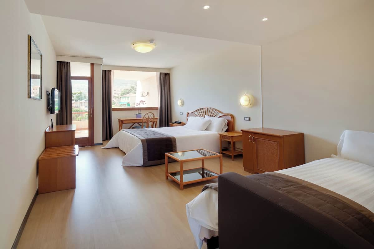Ein Hotelzimmer mit zwei Betten, einem Schreibtisch, einem Stuhl, einem Fernseher und einem Balkon mit Blick.