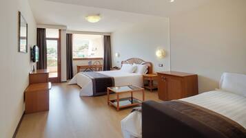 A hotel room with two beds, a desk, a chair, a TV, and a balcony with a view.