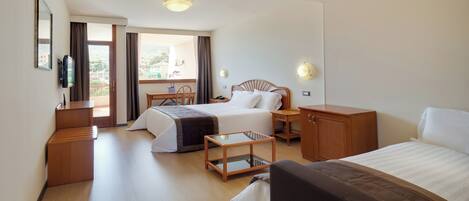Ein Hotelzimmer mit zwei Betten, einem Schreibtisch, einem Stuhl, einem Fernseher und einem Balkon mit Blick.