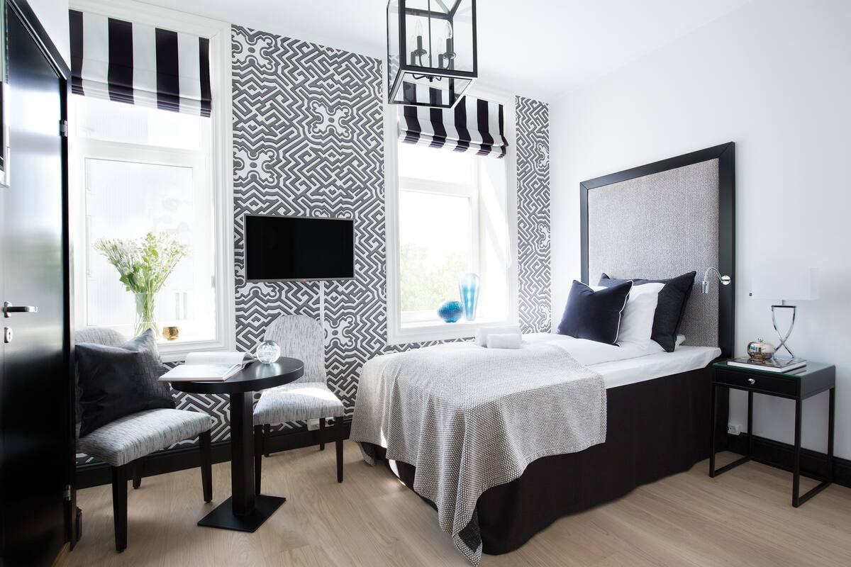 A modern bedroom with a bed, bedside table, chair, and a TV mounted on the wall.
