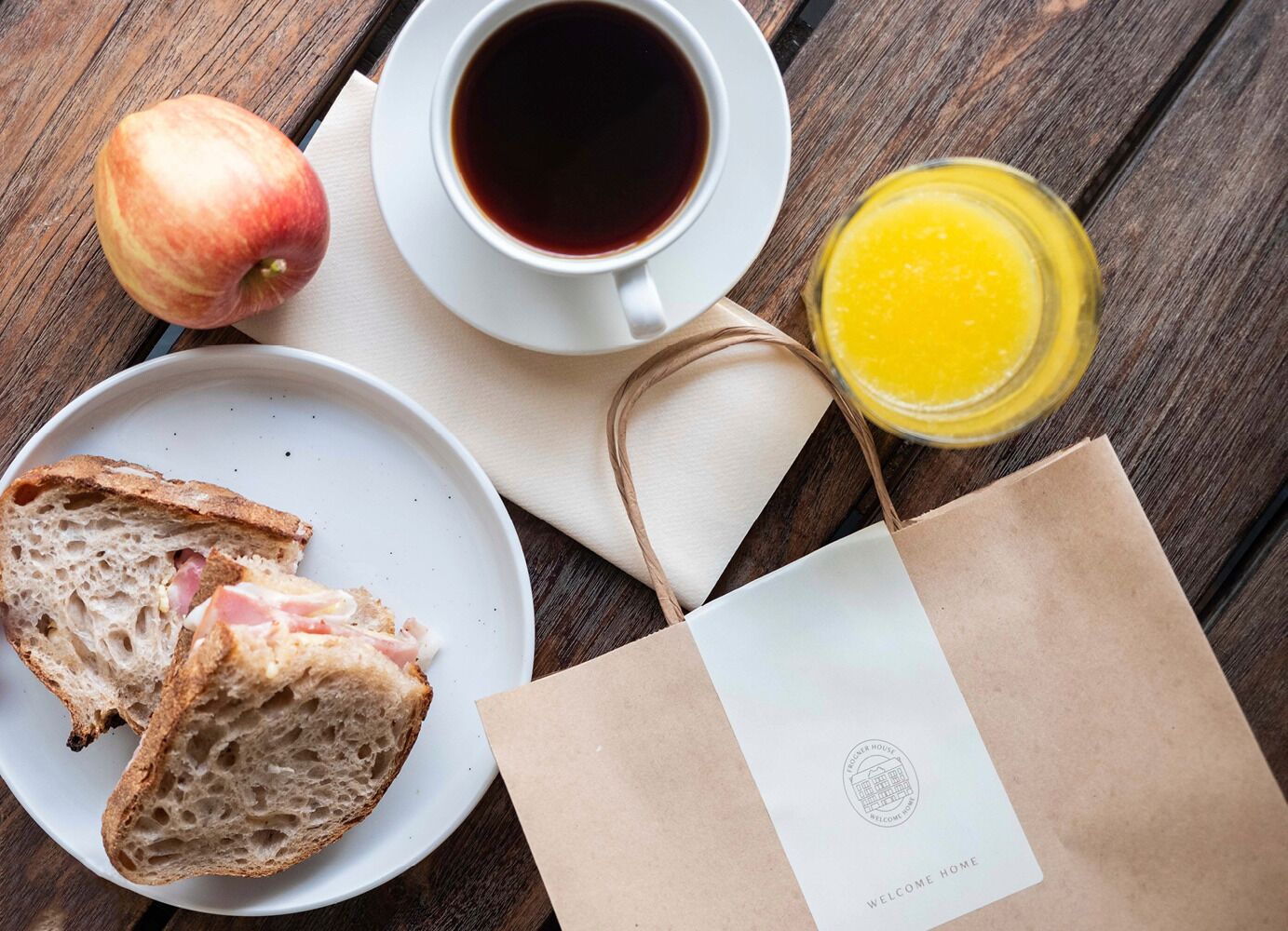 Desayuno con pan, manzana, café y jugo de naranja sobre una mesa de madera.