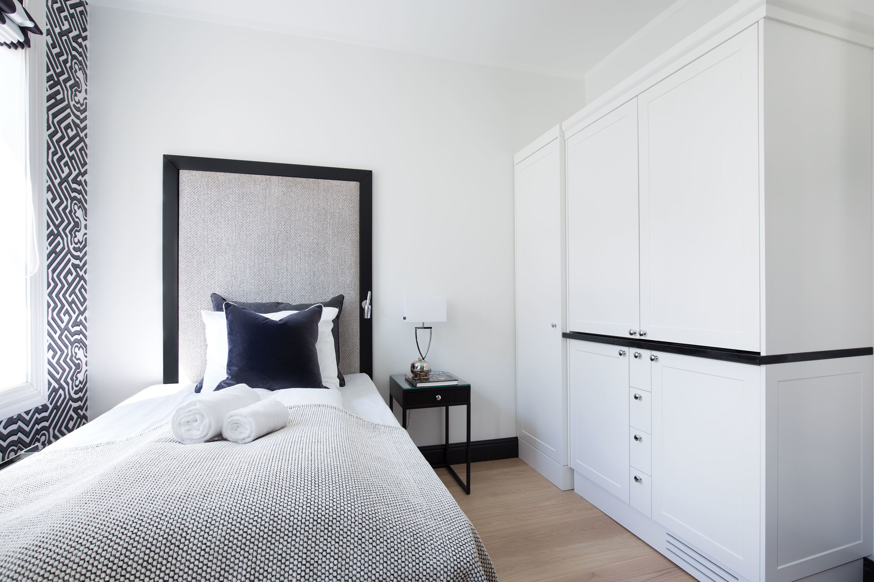 A neatly made bed with a patterned bedspread, a bedside table with a lamp, and a wardrobe with multiple doors.