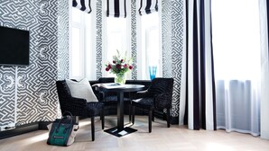 A modern room with patterned wallpaper, a round table, wicker chairs, a vase with flowers, and a TV mounted on the wall. - Frogner House - Bygdøy Allé (Oslo)