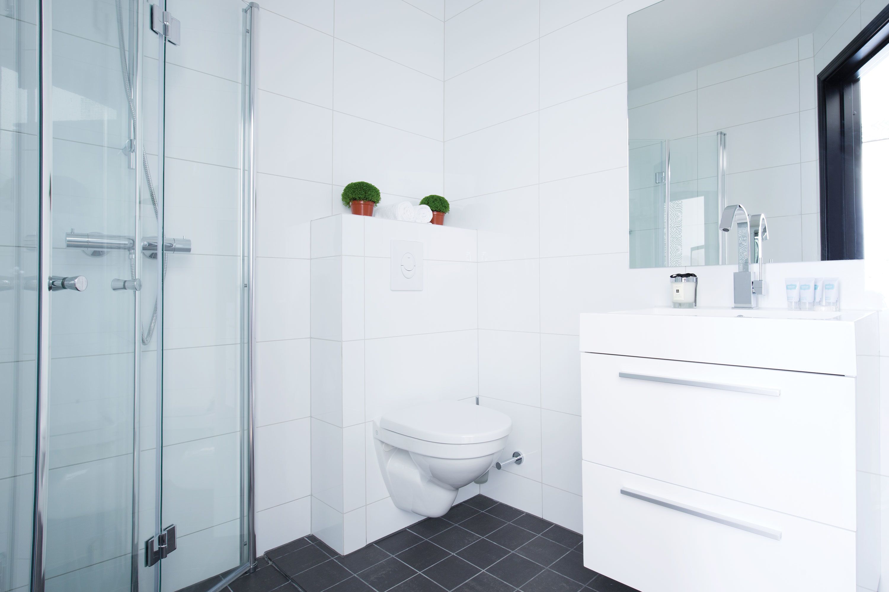 Un baño moderno con cabina de ducha de vidrio, inodoro blanco y tocador blanco con cajones.