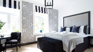 A modern bedroom with a large bed, a side table, a chair, and a window with patterned curtains. - Frogner House - Bygdøy Allé (Oslo)