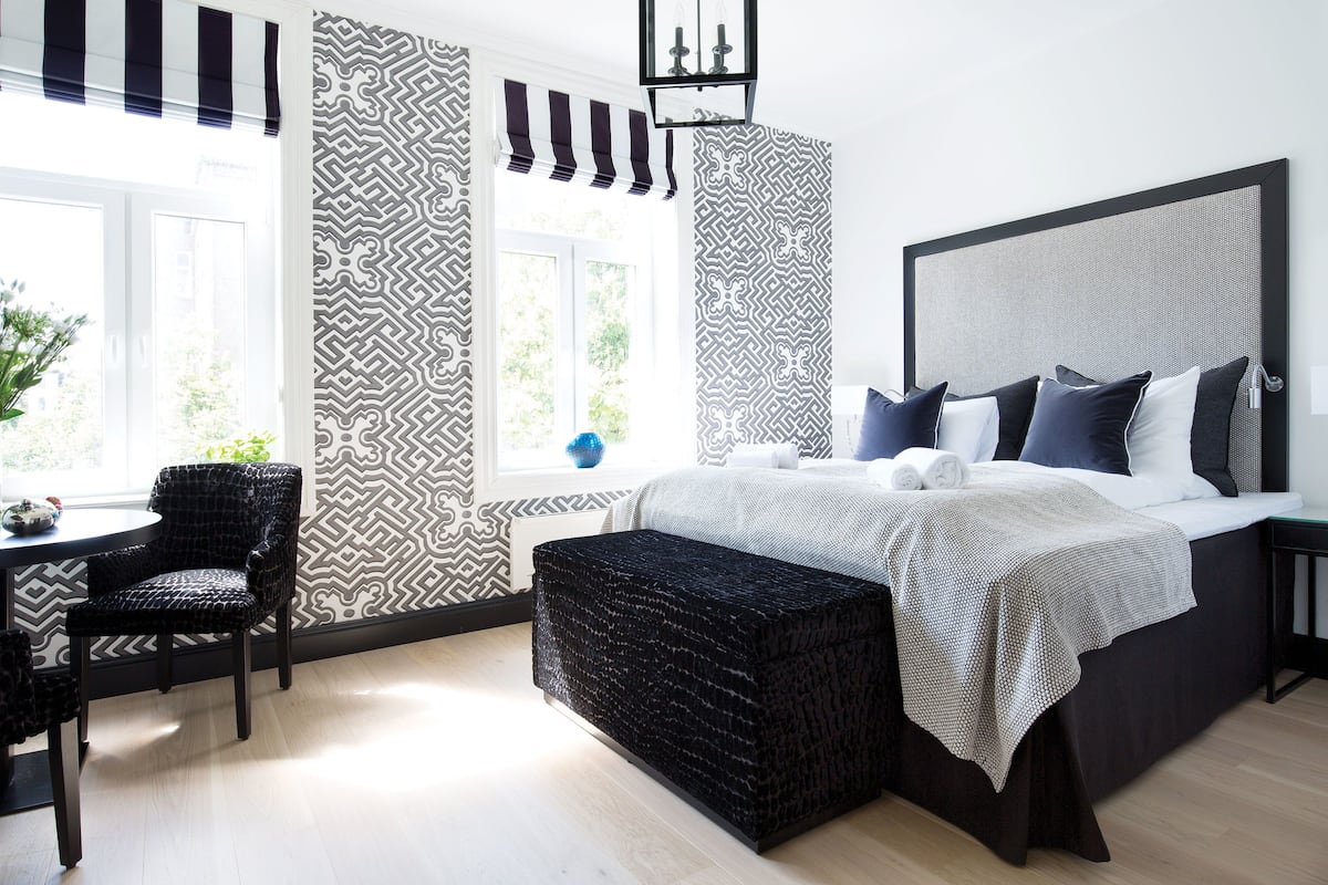 A modern bedroom with a large bed, a side table, a chair, and a window with patterned curtains.