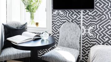Une pièce moderne avec un mur aux motifs noir et blanc, une table ronde sur laquelle se trouve un livre et une sphère de verre, et une fenêtre agrémentée d’un vase de fleurs.