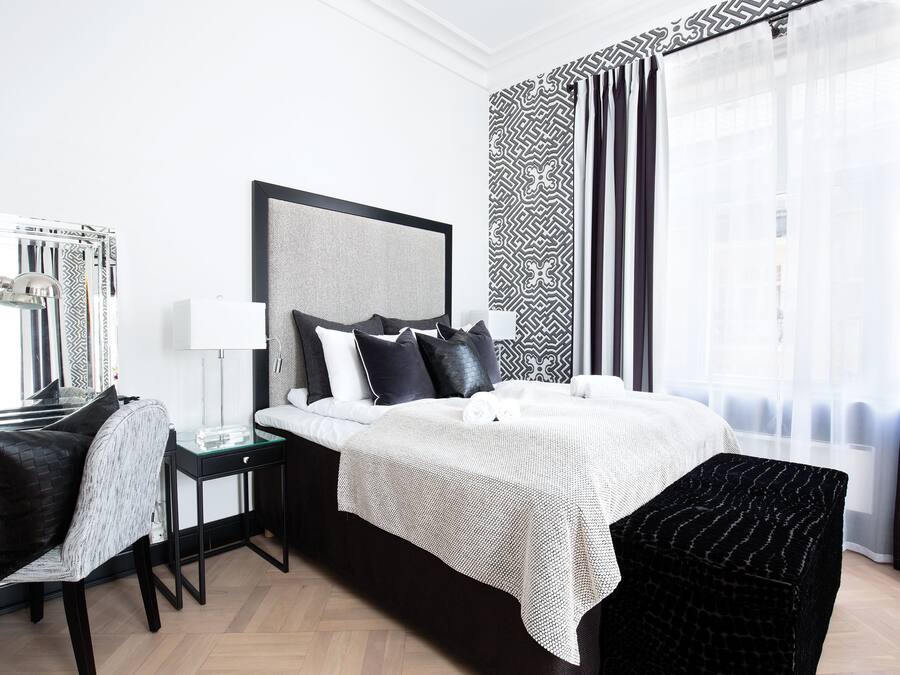 A modern hotel room with a large bed, a bedside table, a chair, and a large window with curtains.