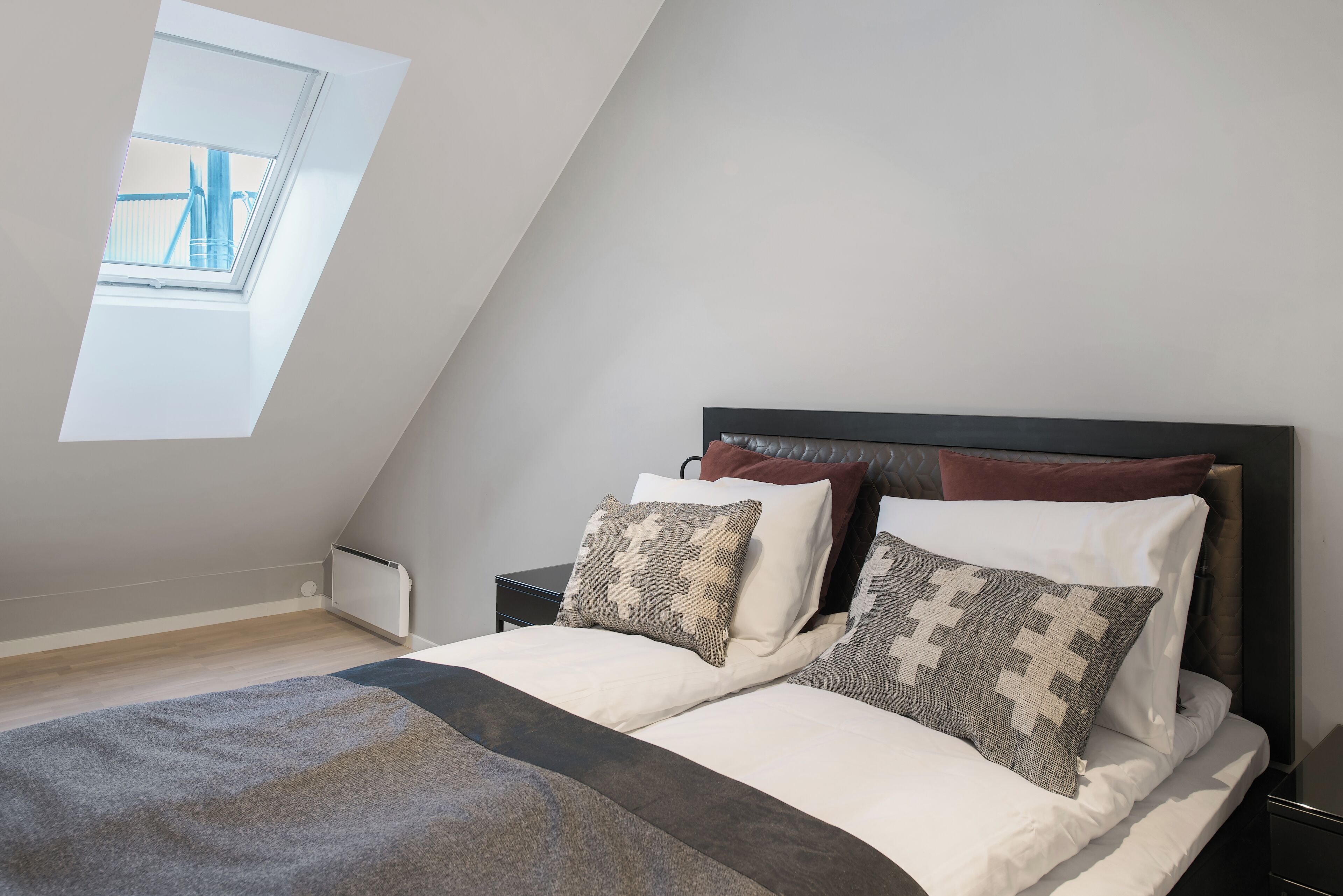 A bedroom with a sloped ceiling, a skylight, a bed with patterned pillows, and a bedside table.