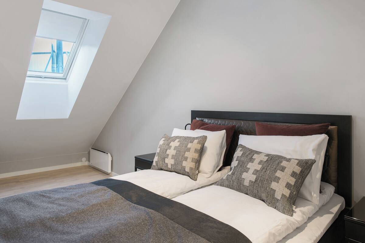 A bedroom with a sloped ceiling, a skylight, a bed with patterned pillows, and a bedside table.