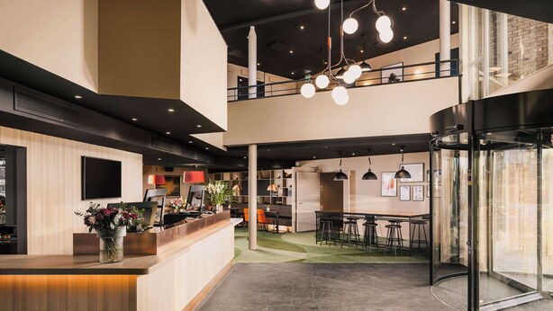 A modern hotel lobby with a reception desk, seating area, and a glass elevator. - Scandic Gardermoen (Ullensaker)