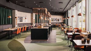 A modern restaurant with a long counter, multiple tables, and chairs. There are pendant lights hanging from the ceiling and a large window on one side. - Scandic Gardermoen (Ullensaker)