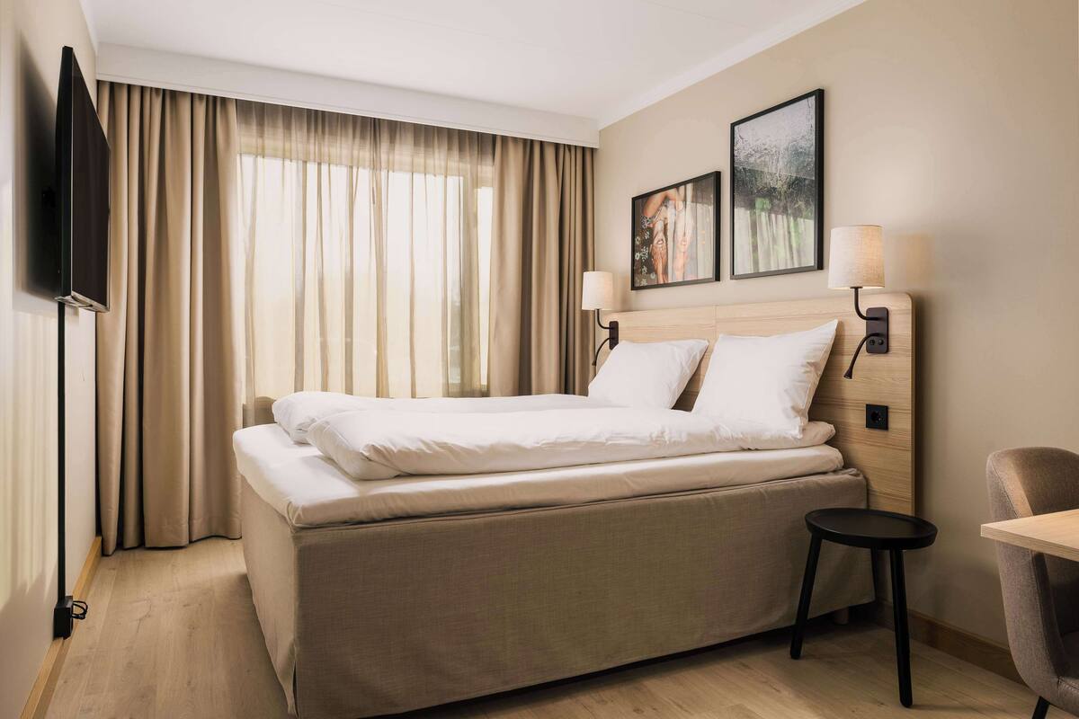 Quarto de hotel com cama, televisão, escrivaninha e cadeira.