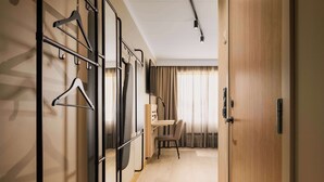 A hotel room with a wooden door, a desk, a chair, and a coat rack with hangers. - Scandic Gardermoen (Ullensaker)