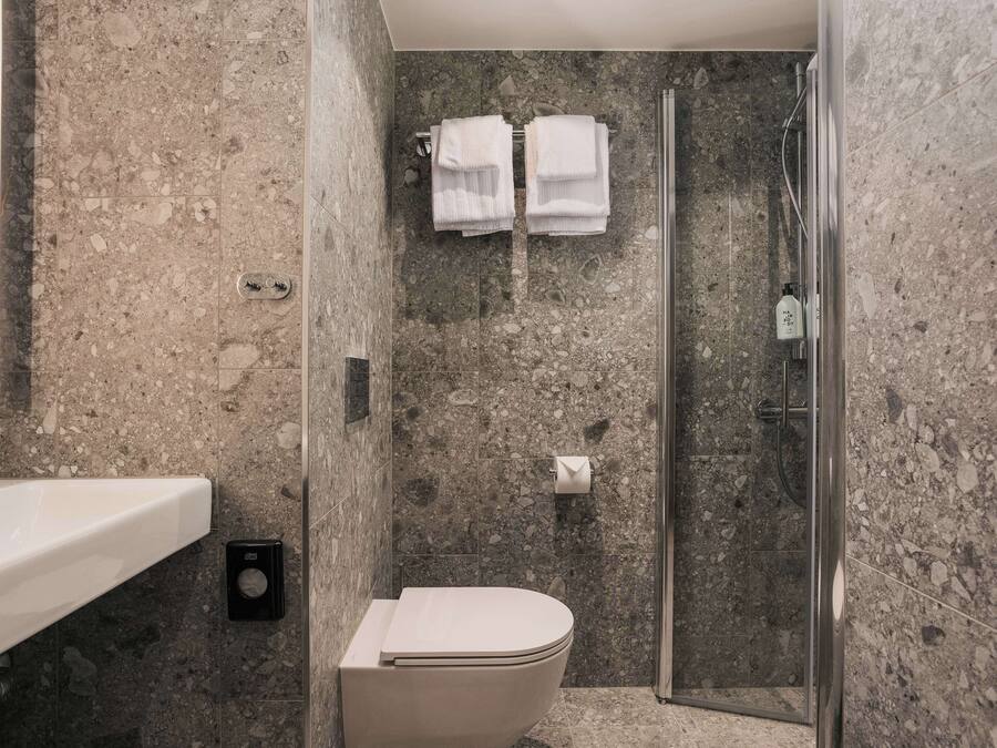 Ein Badezimmer mit Marmorwand, einer Toilette, einer Dusche mit Glastür und zwei Handtüchern an einem Wäscheständer.