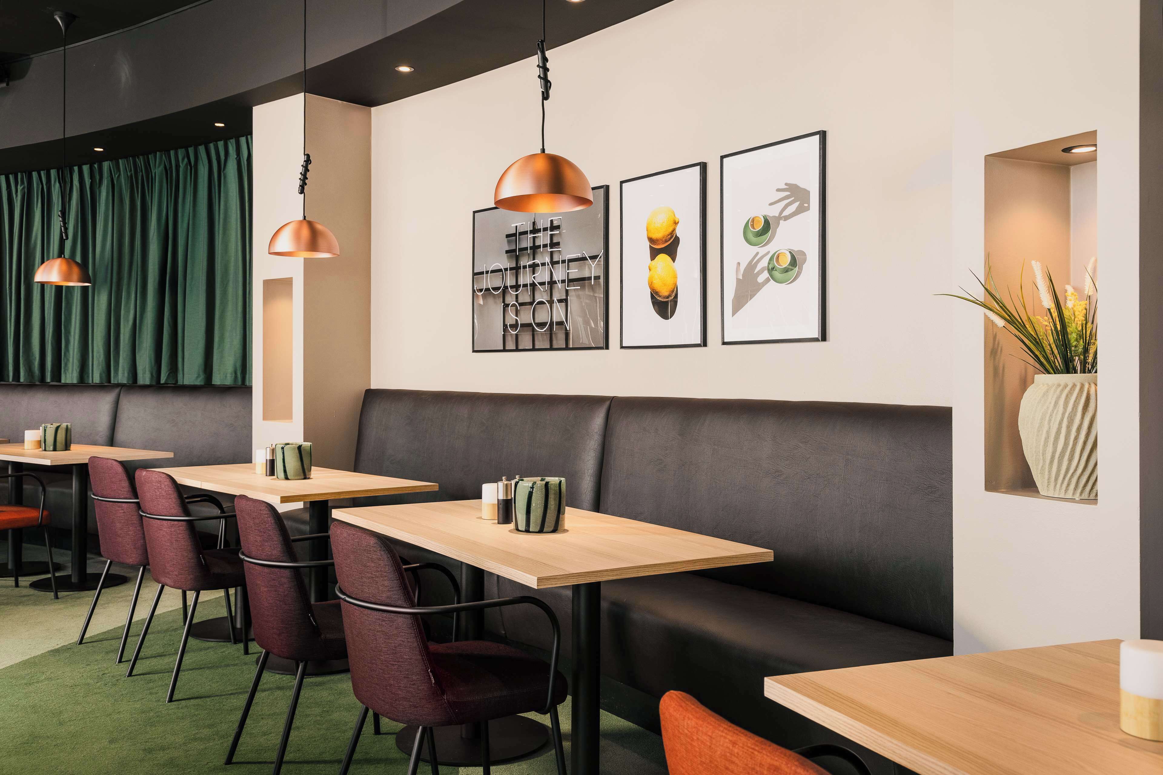 Um restaurante moderno com mesas e cadeiras de madeira, um assento de cabine em couro preto e iluminação pendente.