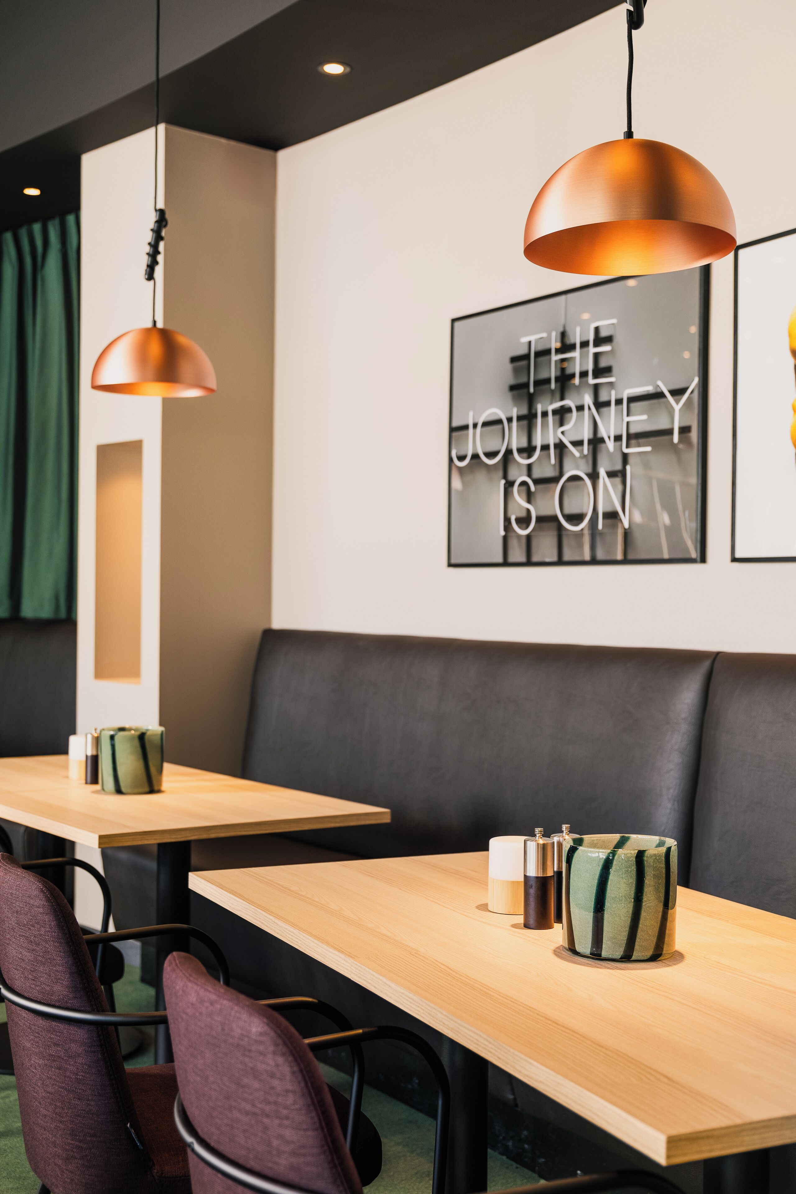 Un área de comedor moderna con mesas de madera, sillas acolchadas e iluminación colgante.