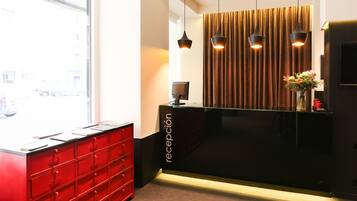 A reception area with a modern design, featuring a black reception desk, red storage units, and a large window offering a view of the street.