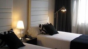 Ein Hotelzimmer mit zwei Betten, einer Nachttischlampe, einem Telefon und einem Fenster mit Vorhängen.