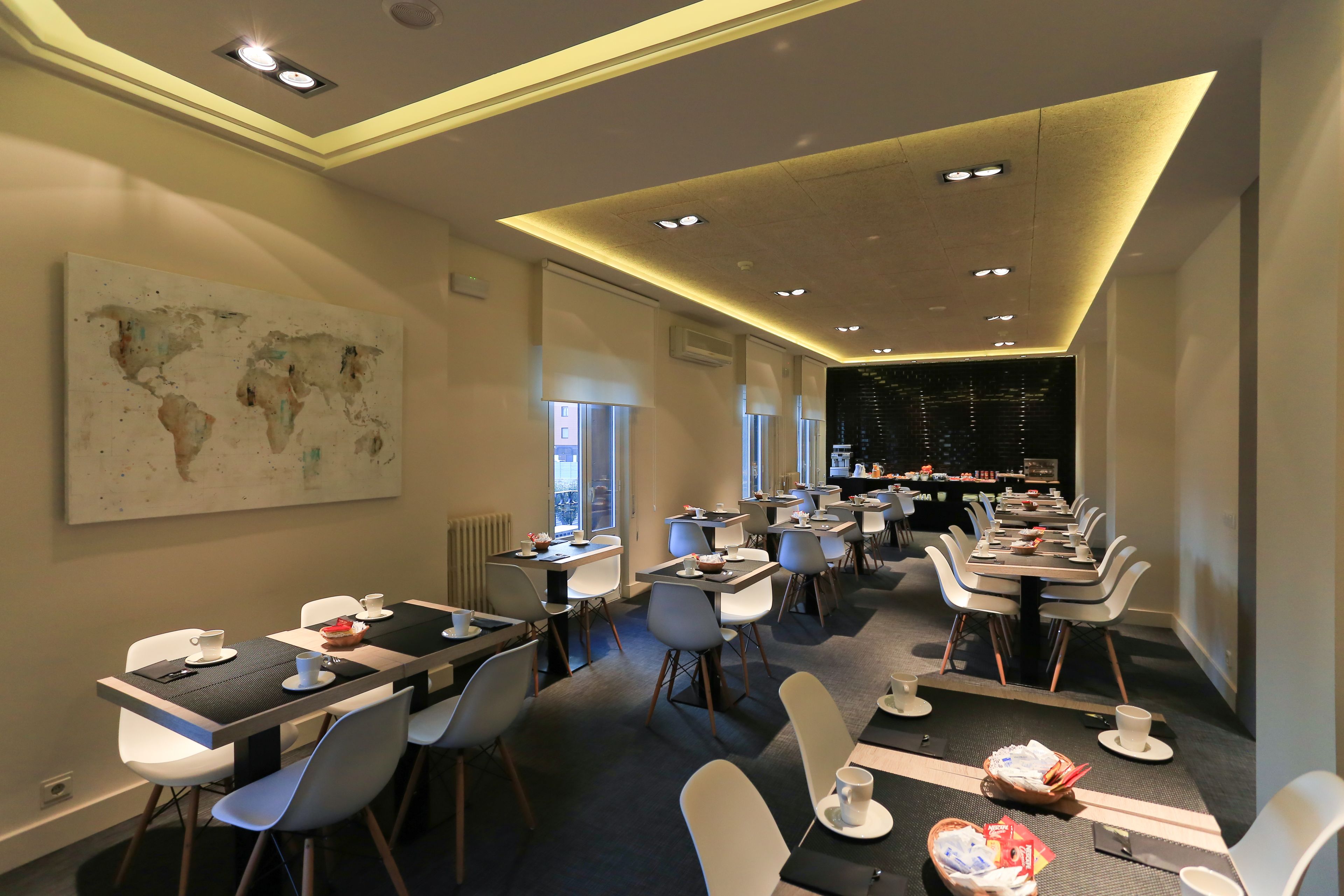 A modern dining area with multiple tables and chairs, a world map on the wall, and a view of the cityscape through large windows.