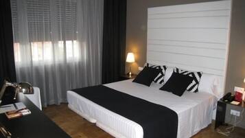 Une chambre d’hôtel avec un lit, un bureau, une lampe et une fenêtre avec des rideaux.