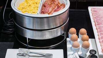 Un plateau de petit-déjeuner comprenant des œufs brouillés, du bacon et des œufs servis dans des ramequins, ainsi que des condiments et des couverts disposés sur une table.
