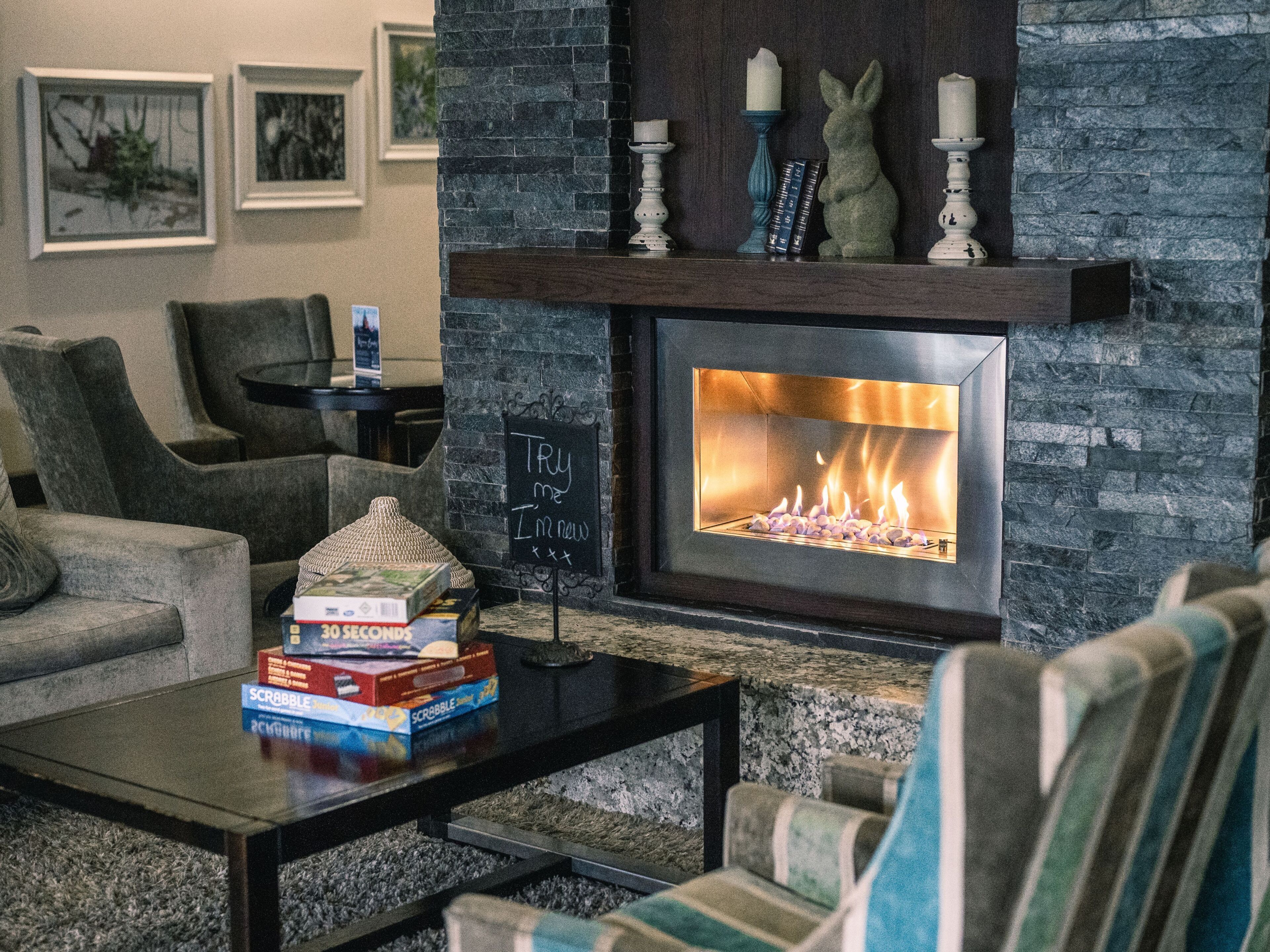 A living room with a stone fireplace, a coffee table with board games, and a sign that reads 'Try me I'm new'.