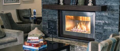 A living room with a stone fireplace, a coffee table with board games, and a sign that reads 'Try me I'm new'.
