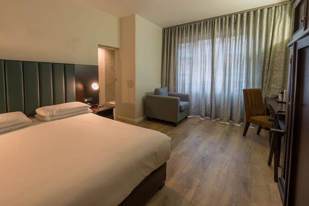 A hotel room with a large bed, a desk, a chair, and a window with curtains.