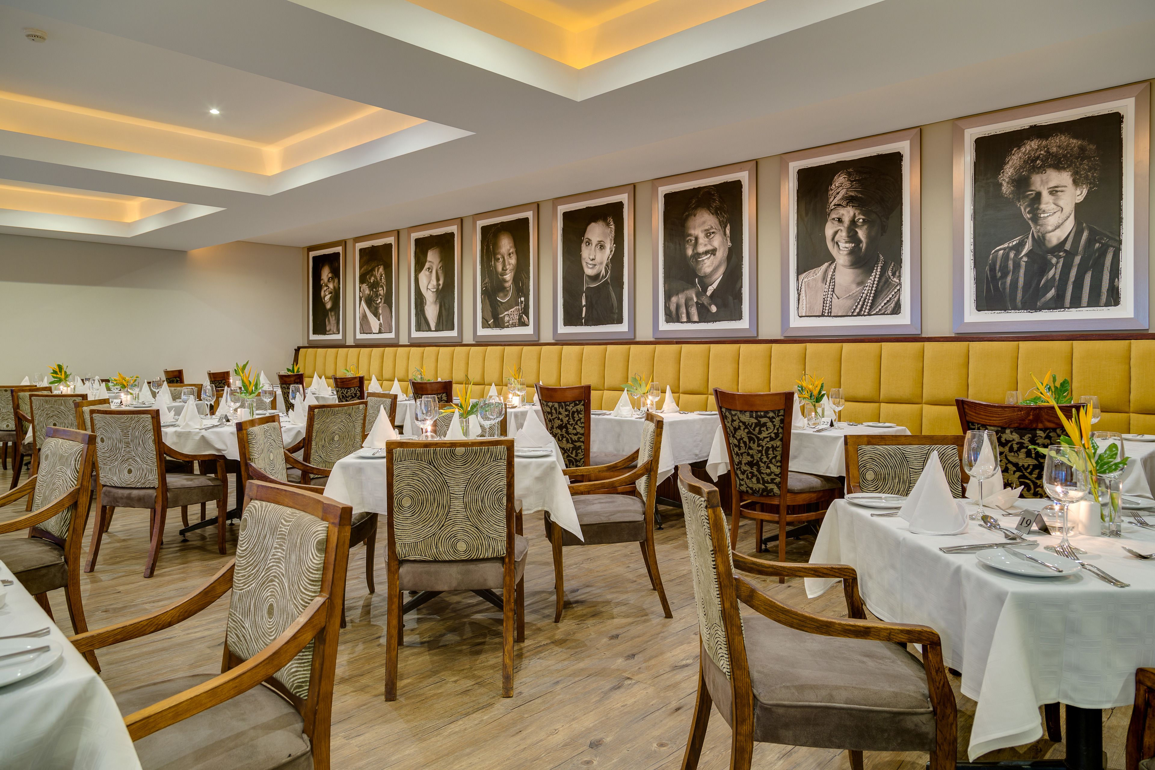 A restaurant with multiple tables set for dining, featuring patterned chairs and a yellow cushioned bench along the wall.