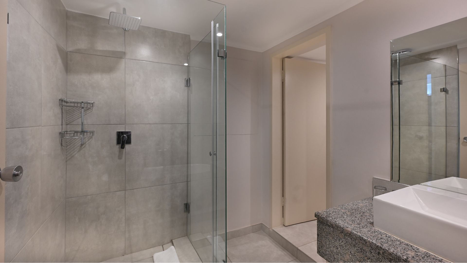 A modern bathroom with a glass-enclosed shower, a vanity with a granite countertop, and a large mirror.