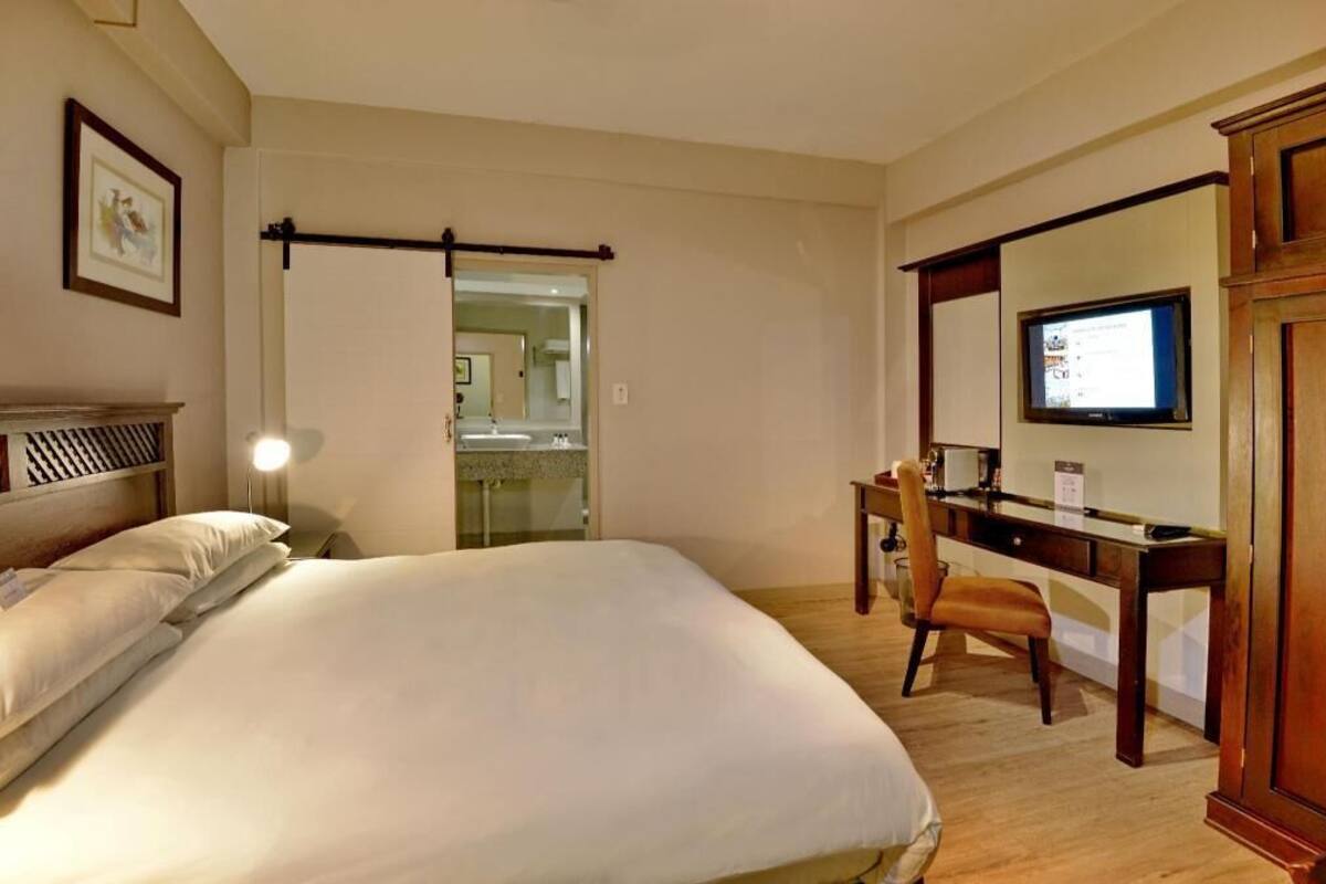 A hotel room with a bed, a desk, a chair, a television, and a mirror.
