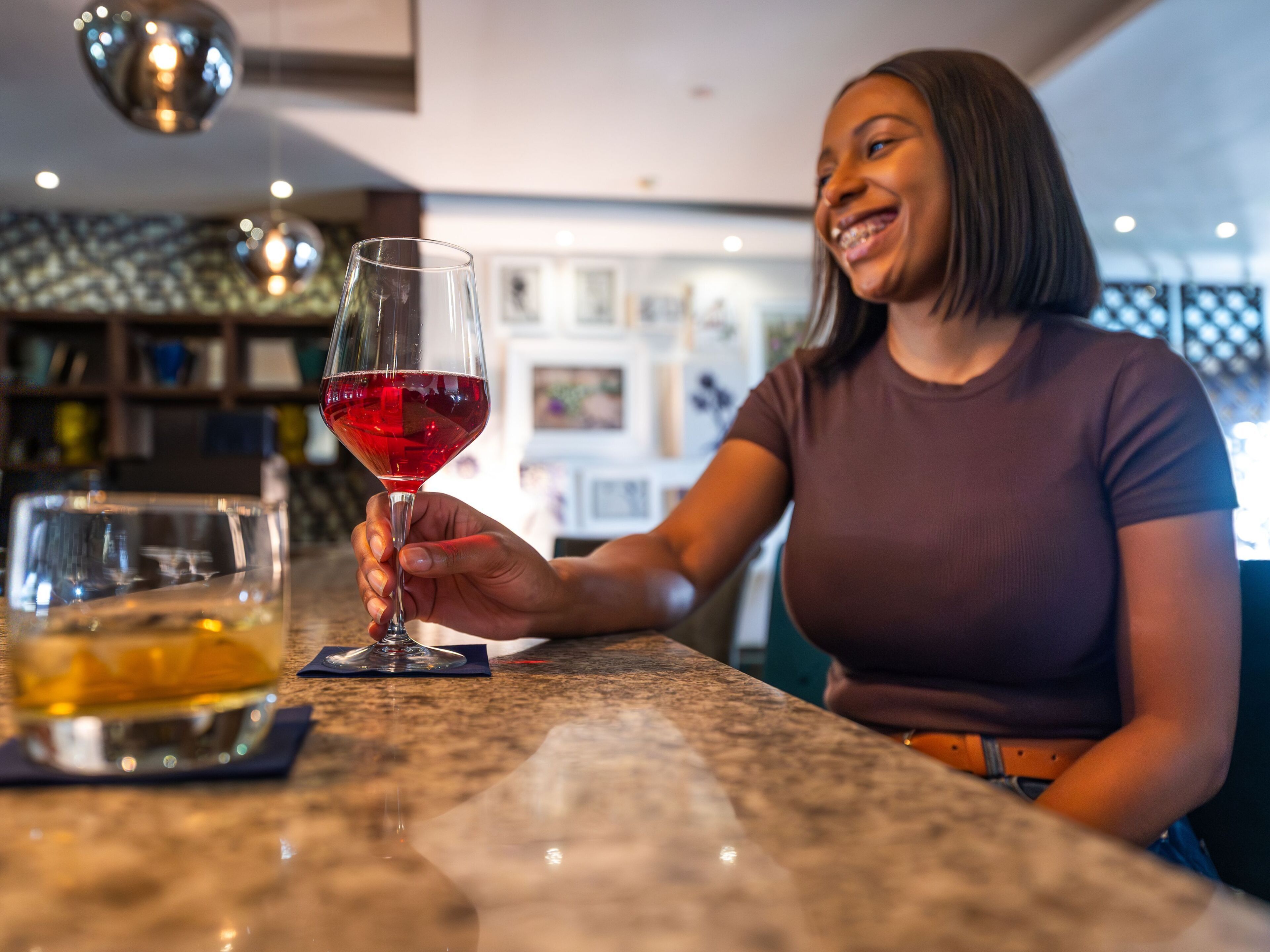 A person holding a glass of red wine at a bar with a marble countertop and a bookshelf in the background.