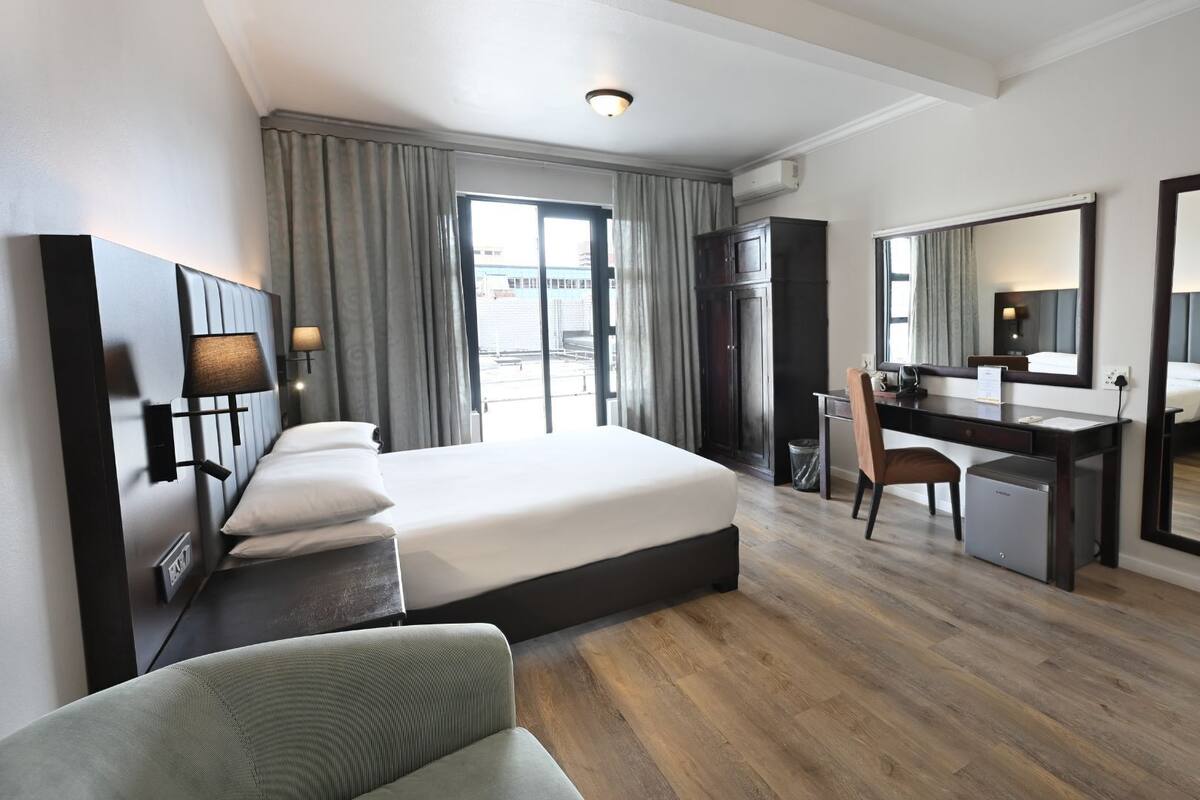 A hotel room with a bed, desk, chair, and a large mirror.