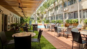 Un patio al aire libre con mesas y sillas, una piscina y un paseo cubierto con ventiladores de techo.