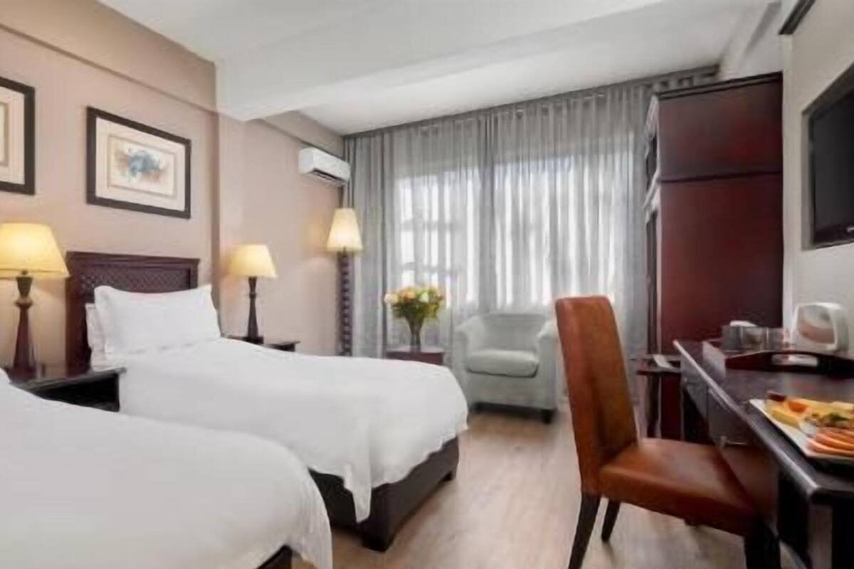 A hotel room with two beds, a desk with a chair, a TV, and a window with curtains.