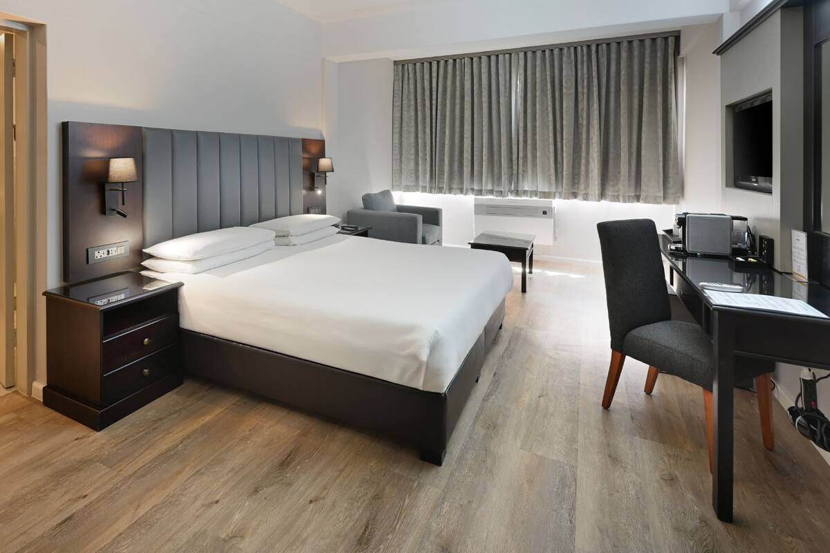 A modern hotel room with a large bed, bedside tables, a desk with a chair, a flat-screen TV, and a bathroom with a sink and mirror.
