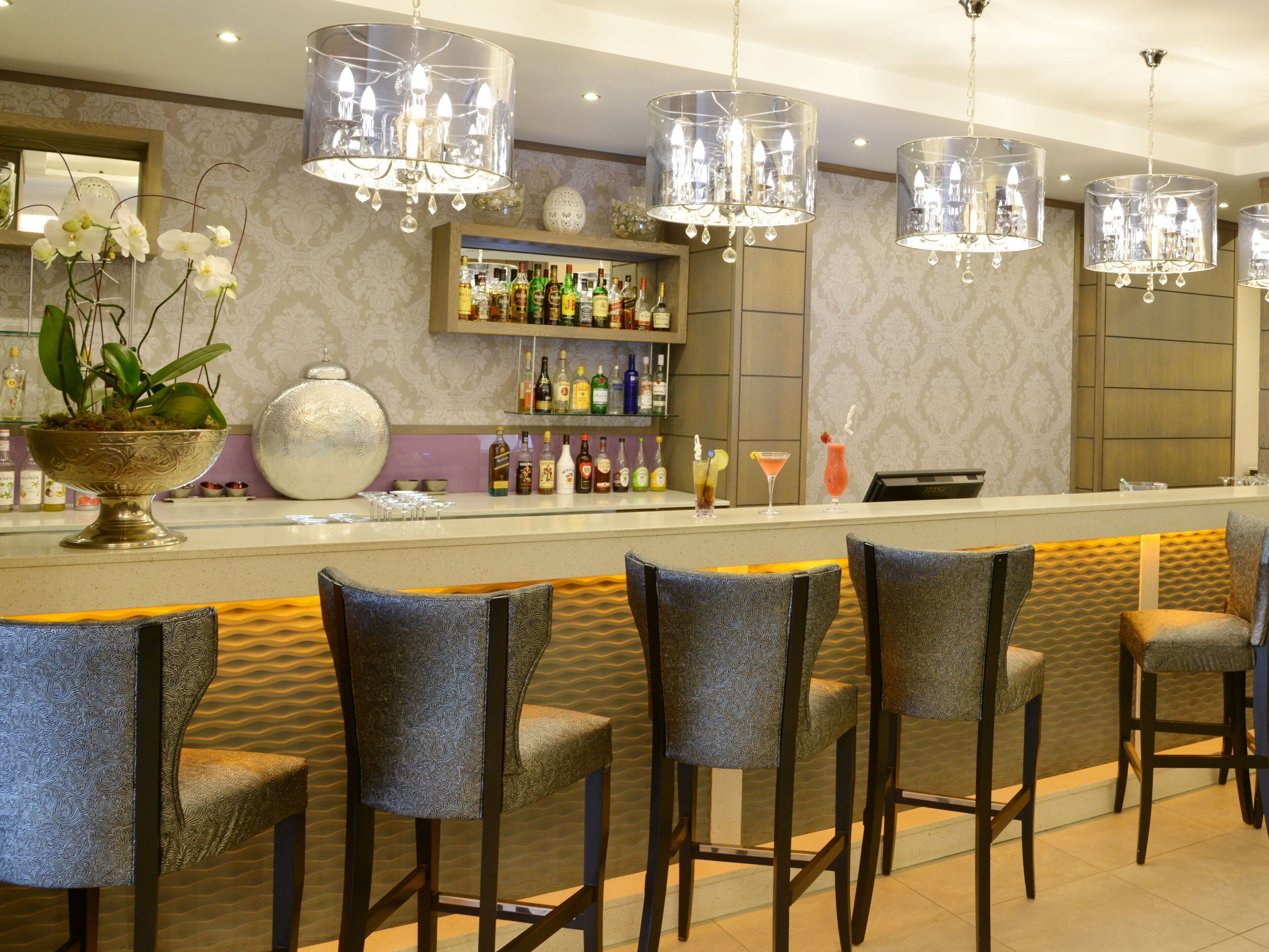 Zona de bar con una barra larga, varios taburetes y candelabros de cristal colgantes.
