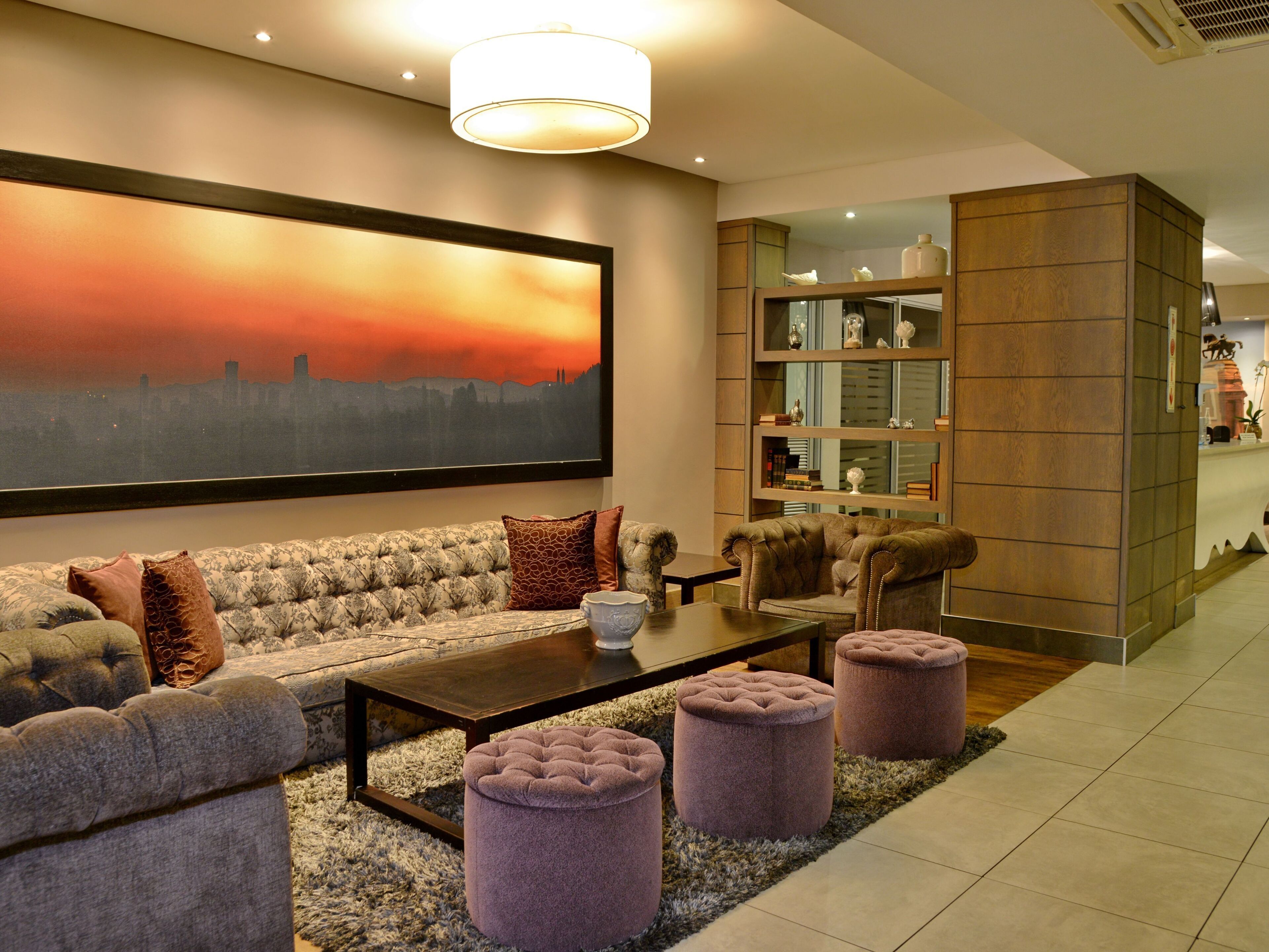 Un salon moderne avec un canapé, des poufs, une table basse et un grand tableau.