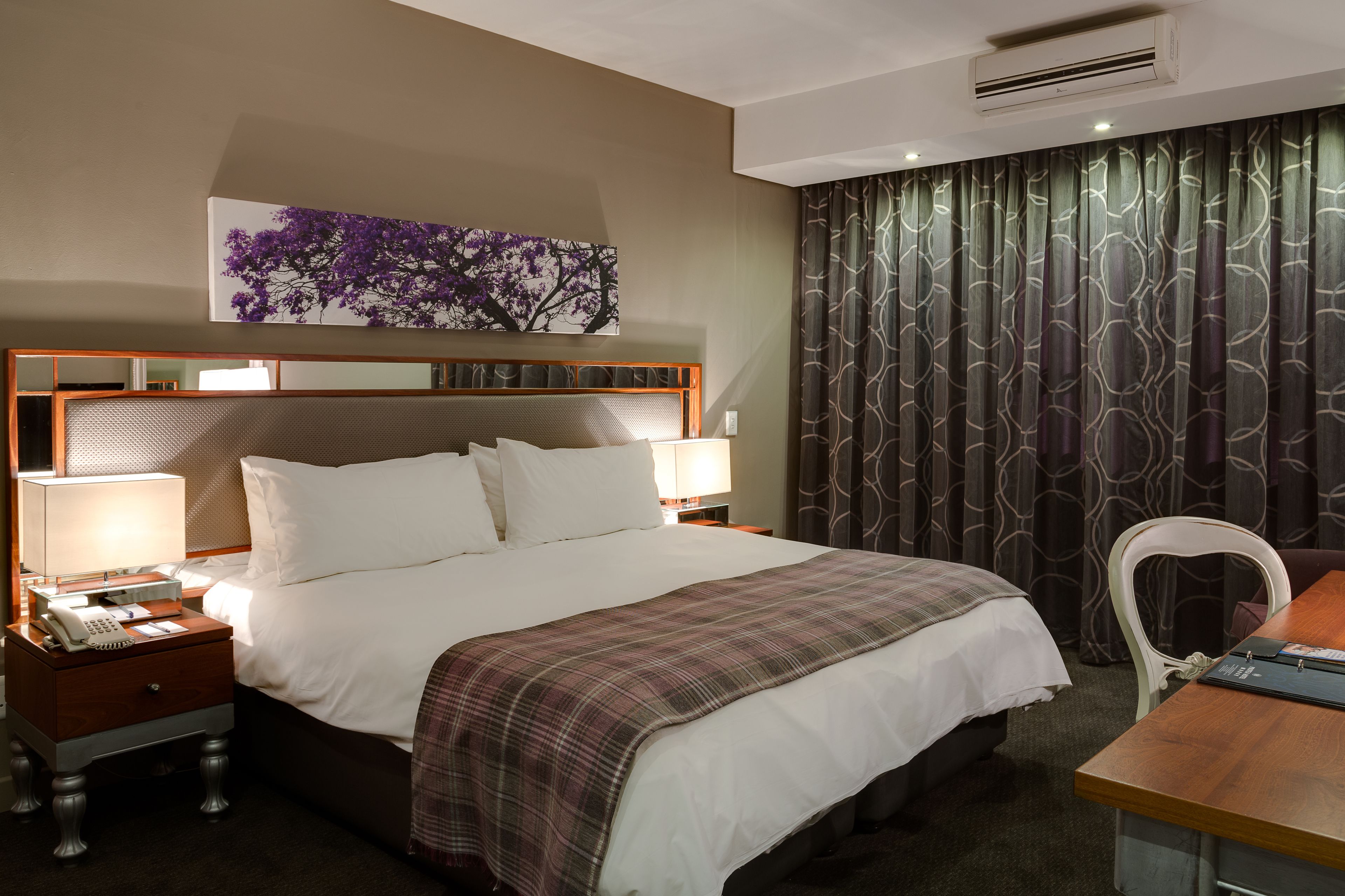 Habitación de hotel con una cama grande, una mesita de noche con lámpara, una silla y un escritorio.