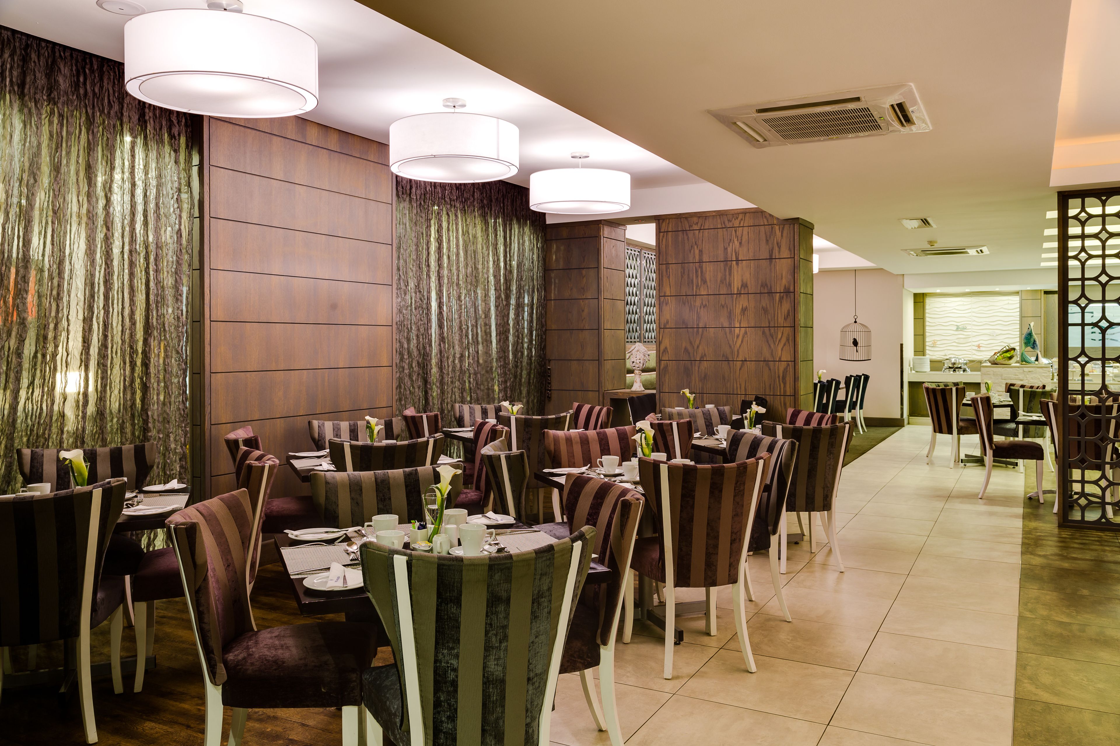 Un restaurant doté de nombreuses tables et chaises, d’un mur décoratif et de luminaires suspendus.