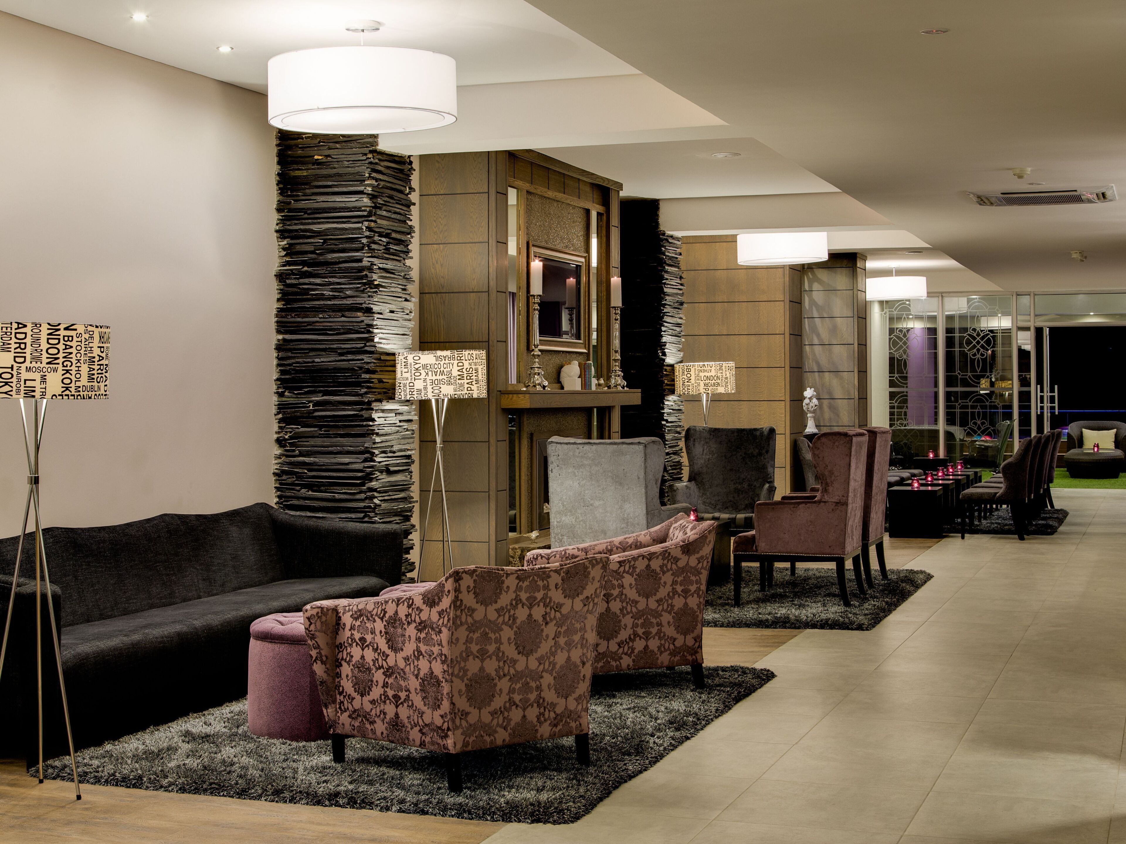 A modern lobby with a sofa, armchairs, a fireplace, and a large mirror.