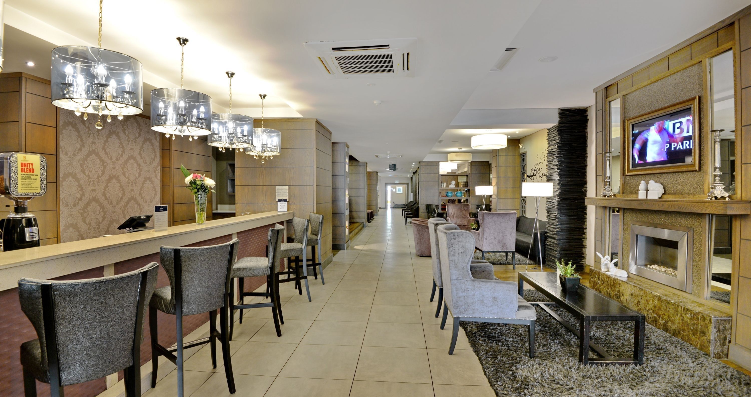 A hotel lobby with a reception desk, bar area, seating, and a TV screen.