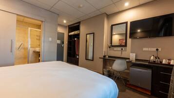 Quarto de hotel com uma cama grande, uma escrivaninha com cadeira, espelho, televisão e uma cozinha compacta.