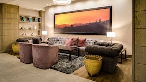 Una sala de estar moderna con un sofá gris, dos sillones, una mesa de centro y un cuadro grande de un horizonte al atardecer.