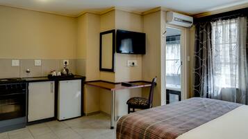 A hotel room with a bed, a desk, a chair, a kitchenette, and an air conditioning unit.