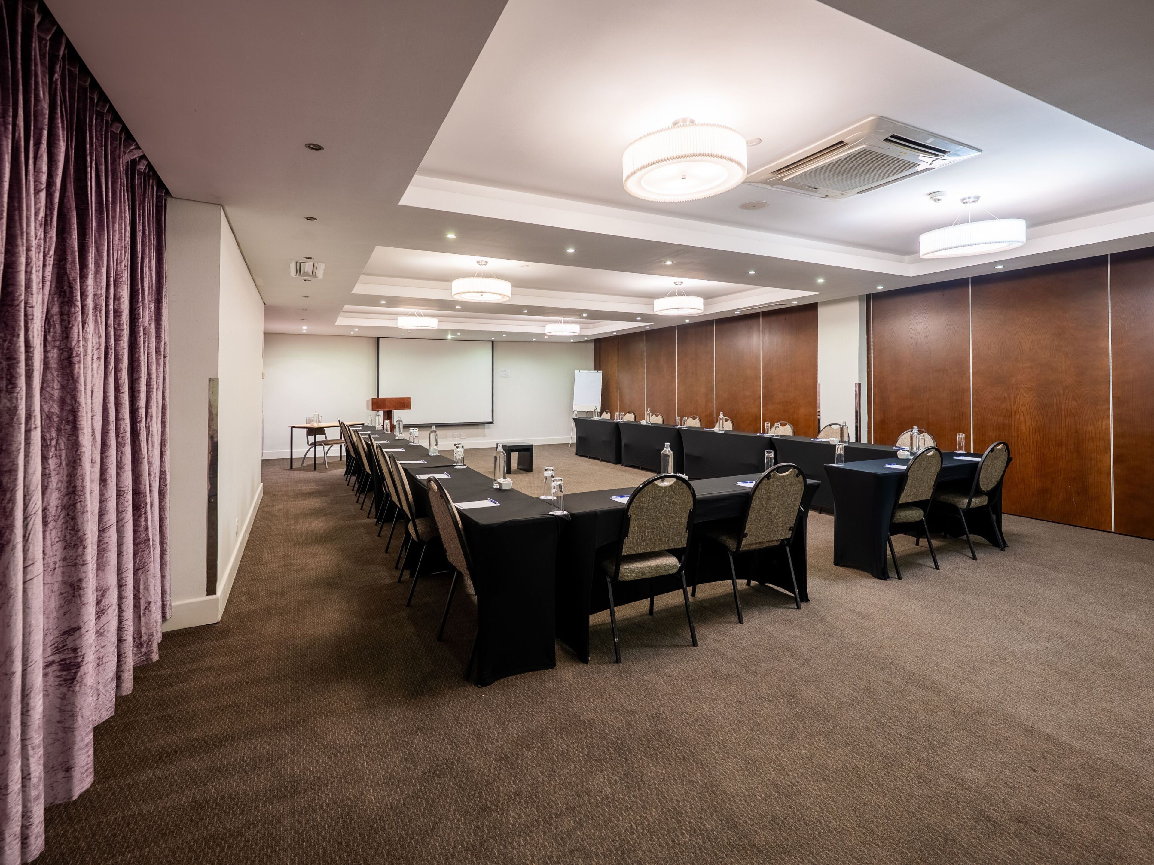 A conference room with a long table, chairs, a projector screen, and a whiteboard.