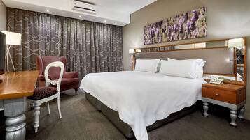 Ein Hotelzimmer mit einem großen Bett, einem Schreibtisch, einem Stuhl und einem Nachttisch mit Telefon.